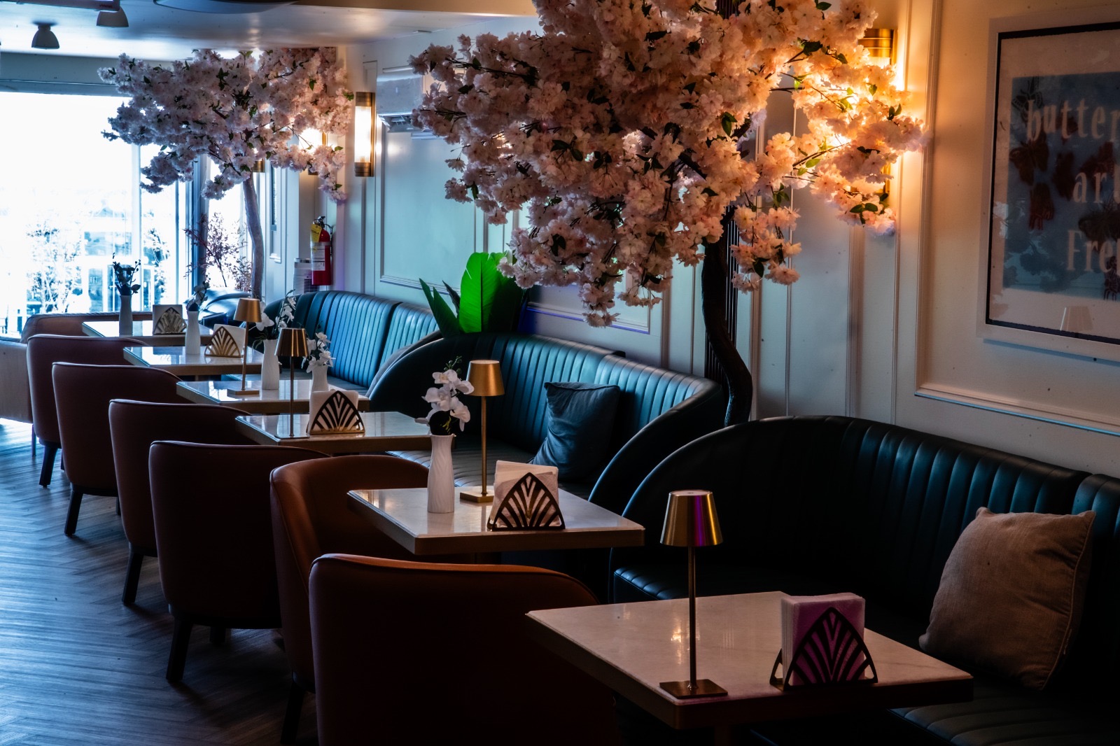 Long teal banquette and tan chairs beneath blossom trees at Yorkville Lounge